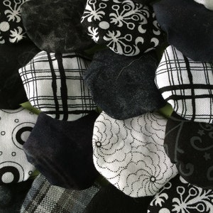 May include: An assortment of black and white fabric pieces with various patterns, including floral, plaid, and geometric designs. The pieces are arranged closely together, creating a textured and visually interesting display. The fabrics appear to be cotton or a similar material.