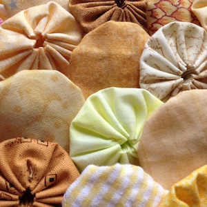 May include: Close-up of a patchwork quilt with various yellow and tan fabric circles. The circles are arranged closely together, creating a textured surface. Some circles have a gathered center, while others are flat.