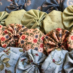 May include: Close-up of a handmade quilt or decorative item. The quilt features a variety of fabric circles in shades of red, blue, green, and peach. Some circles have floral patterns, while others have simple designs.