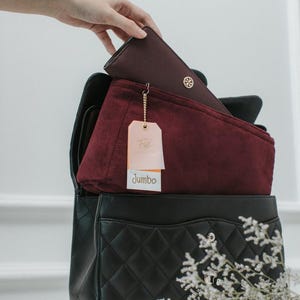 May include: A black quilted handbag with a burgundy felt insert and a gold tag that says "Jumbo".
