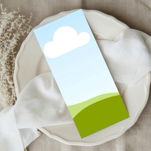 Peut inclure: Une carte rectangulaire avec un motif de ciel et de nuage, présentant un nuage blanc sur un fond dégradé bleu clair. Le bas de la carte présente un motif de colline verte. La carte est présentée sur une assiette blanche avec un tissu blanc.