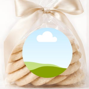 May include: A clear cellophane bag tied with a cream-colored ribbon, filled with several light-colored cookies. A round sticker with a blue sky, white cloud, and green hills is on the front of the bag. The cookies are stacked neatly.