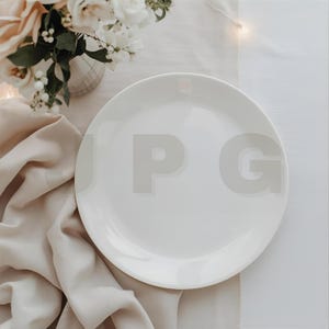 Puede incluir: Un plato de cerámica blanca sobre un mantel de lino beige, junto a un jarrón con flores blancas y melocotón. La escena está iluminada con luz suave y natural, creando una estética limpia y elegante. El plato es redondo y parece sin usar.