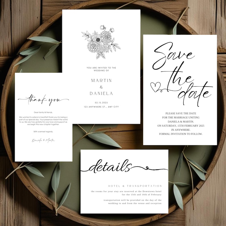 May include: A collection of white wedding stationery cards with black text. The cards include a floral invitation, a save-the-date card, a thank you card, and a details card. The cards are arranged on a wooden tray with greenery.