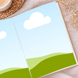 May include: Open book with a landscape illustration. The pages display a blue sky with white clouds and green rolling hills. The book is open on a light-colored surface, with a cup of coffee and decorative elements in the background.