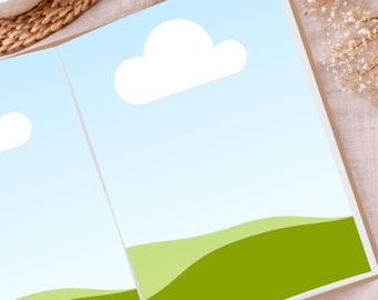 May include: Open book with a landscape illustration. The pages display a blue sky with white clouds and green rolling hills. The book is open on a light-colored surface, with a cup of coffee and decorative elements in the background.