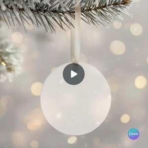 Peut inclure: Une boule de Noël blanche et ronde, vierge, avec un ruban crème pour la suspendre. L'ornement est suspendu à une branche de conifère givrée, avec un arrière-plan flou de lumières bokeh douces et chaudes.