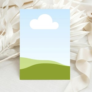 Può includere: Un biglietto di auguri con un design paesaggistico con cielo blu, nuvola bianca e colline verdi. Il biglietto è circondato da elementi decorativi bianchi e un rotolo di nastro.