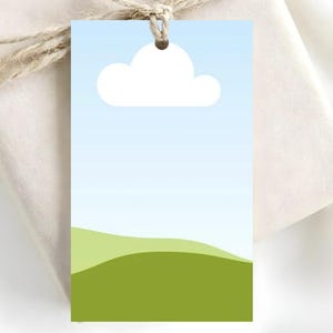 May include: A rectangular gift tag with a sky and landscape design. The top portion features a light blue gradient with a white cloud. The bottom has green rolling hills. A natural twine string is attached.