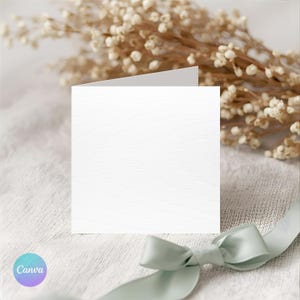May include: A blank white card with a textured surface, open to show a clean interior. A pale green ribbon is tied in a bow at the bottom right. Dried flowers in the background provide a soft, neutral aesthetic.