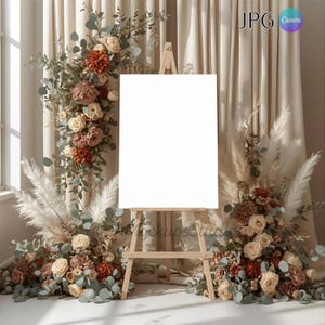 Puede incluir: Un caballete de madera con un lienzo blanco en blanco se encuentra frente a un telón de fondo de cortinas beige y arreglos florales. Las flores incluyen rosas, hierba de la pampa y eucalipto.