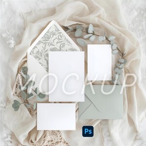 May include: A stationery mockup featuring a white envelope with a floral patterned interior, blank cards, and a sage green envelope. Eucalyptus sprigs and fabric add a natural, elegant touch. The word "MOCKUP" is overlaid on the image.