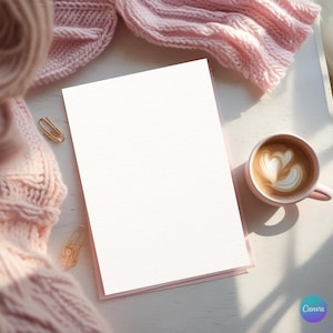 Puede incluir: Una tarjeta blanca en blanco con un borde rosa descansa sobre una superficie blanca, junto a una taza rosa de arte latte y una bufanda de punto rosa. También se ven clips dorados y un logotipo de Canva.