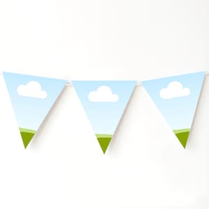 May include: A string of three triangular pennant flags. Each flag features a blue sky background with a white cloud and a green grassy area at the bottom. The flags are strung together with a white string.