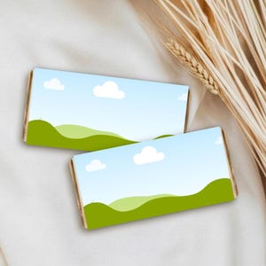 May include: Two rectangular bars with a landscape design featuring green hills, a blue sky, and white clouds. The bars have a wooden border and are set against a white fabric background with wheat stalks.