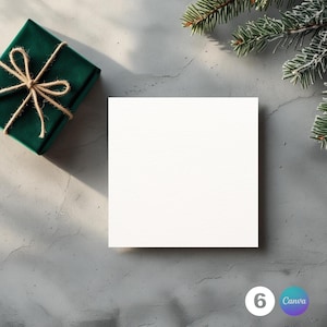 Könnte beinhalten: Eine quadratische weiße Karte liegt auf einer grauen Oberfläche, neben einer verpackten dunkelgrünen Geschenkbox, die mit Bindfaden verschnürt ist. Ein Zweig mit immergrünen Ästen befindet sich in der oberen rechten Ecke. Die Zahl 6 und das Wort Canva befinden sich unten rechts.
