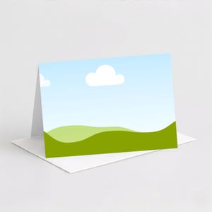 May include: A blank greeting card featuring a landscape scene with a blue sky, white clouds, and green rolling hills. The card is propped up on a white envelope, ready for a personalized message.