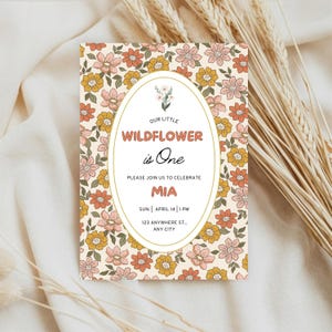 K&ouml;nnte beinhalten: Eine rechteckige Einladungskarte mit cremefarbenem Hintergrund und einem wiederkehrenden Muster aus rosa, orangefarbenen und gelben Blumen. Ein zentrales wei&szlig;es Oval enth&auml;lt den Text: Our Little Wildflower is One, Please Join Us to Celebrate, Mia, Sun. April 14, 1 PM, 123 Anywhere St., Any City.