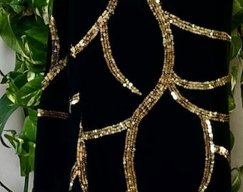 May include: Black fabric with gold sequin embellishments in a branching pattern. The fabric is draped over a wooden hanger, with green foliage in the background. The design is elegant and eye-catching.