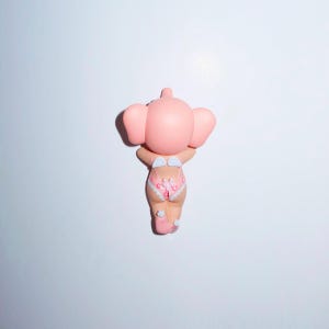K&ouml;nnte beinhalten: Rosa Elefantenfigur, von hinten gesehen. Die Figur tr&auml;gt rosa Unterw&auml;sche mit Blumenmuster. Der Elefant h&auml;lt die Arme hoch, die Ohren sind gespreizt. Wei&szlig;er Hintergrund.
