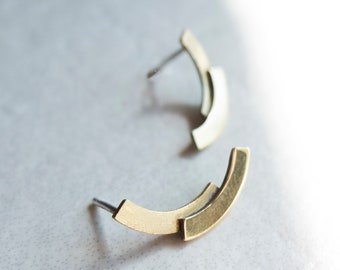 May include: A pair of gold-toned stud earrings, each featuring two stacked, curved metal bars in a crescent shape. The earrings have a smooth, metallic finish and include a standard post backing for secure attachment to the earlobe.