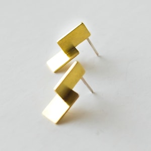 May include: A pair of gold geometric earrings with a zig-zag design. The earrings are made of brass and have a simple, modern style.