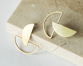 May include: A pair of gold-toned geometric earrings with a half-circle design. The earrings are made of metal and have a minimalist style.