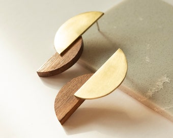 Può includere: Un paio di orecchini moderni con un design a semicerchio. Gli orecchini combinano un elemento in legno marrone scuro con un semicerchio in metallo color oro a contrasto. Gli orecchini sono a lobo.