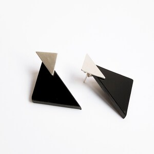 Puede incluir: Un par de pendientes geom&eacute;tricos con formas triangulares negras y detalles plateados.