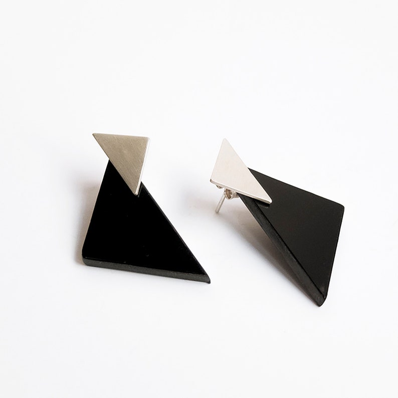 Puede incluir: Un par de pendientes geom&eacute;tricos con formas triangulares negras y detalles plateados.