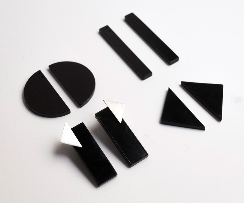 Puede incluir: Un conjunto de pendientes geom&eacute;tricos negros, que incluyen c&iacute;rculos, tri&aacute;ngulos y rect&aacute;ngulos. Algunos pendientes tienen un acento triangular plateado.
