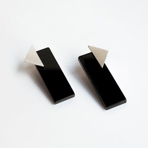 Puede incluir: Un par de pendientes rectangulares negros con detalles triangulares plateados.