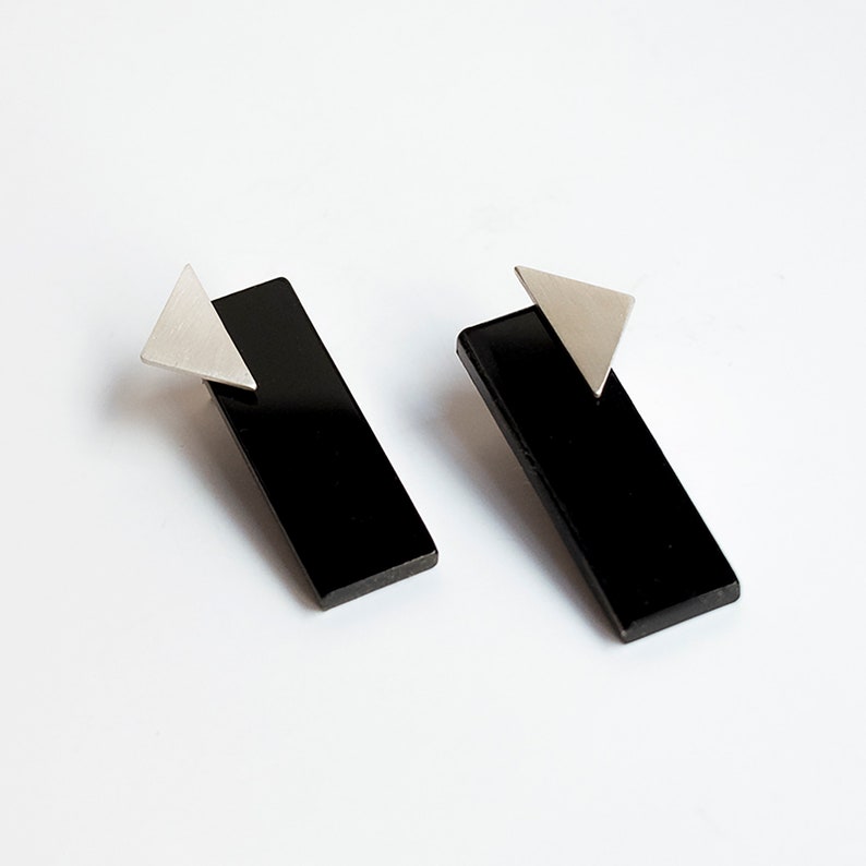 Puede incluir: Un par de pendientes rectangulares negros con detalles triangulares plateados.