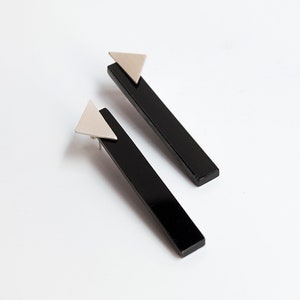 Puede incluir: Un par de pendientes negros y plateados. Cada pendiente tiene una pieza rectangular negra larga con un tri&aacute;ngulo plateado en la parte superior.