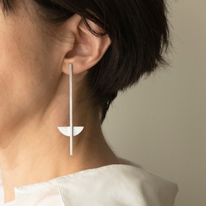 Op de afbeelding: Een paar zilveren oorbellen met een lange, dunne staaf en een halve cirkelvorm aan de onderkant.