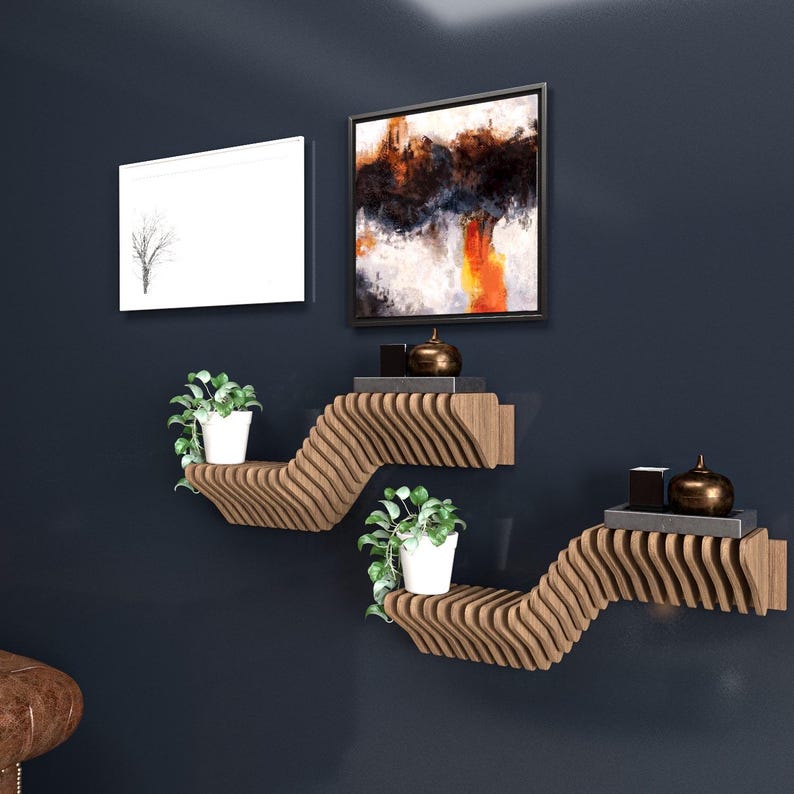 Pu&ograve; includere: Due mensole a muro in legno con un design ondulato. Le mensole sono montate su una parete blu scuro. La mensola superiore ha una piccola pianta in vaso e due oggetti decorativi. La mensola inferiore ha una piccola pianta in vaso e un piccolo oggetto rettangolare.