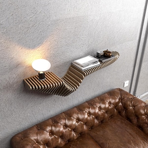 Pode incluir: Uma prateleira de parede de madeira com um design ondulado &uacute;nico. A prateleira est&aacute; montada em uma parede cinza e tem uma pequena l&acirc;mpada e livros.