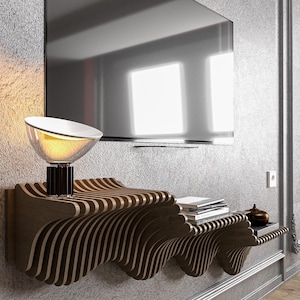 Puede incluir: Una estantería de pared de madera moderna con un diseño único en forma de onda. La estantería está hecha de múltiples capas de madera, creando un efecto tridimensional. Una lámpara y libros se muestran en la estantería.