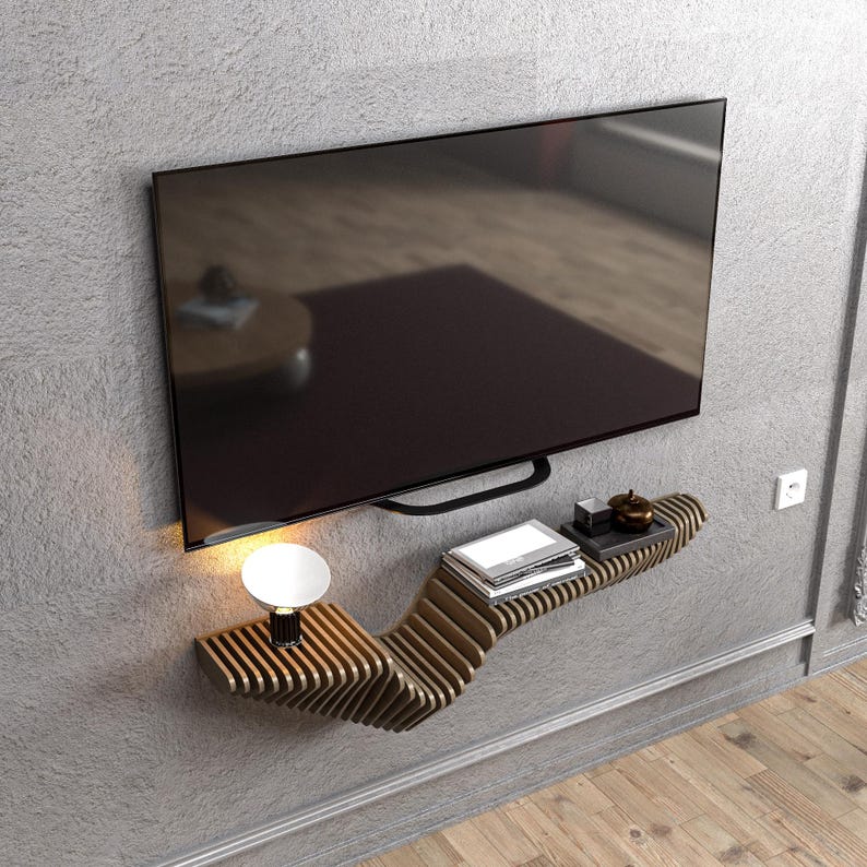 Pode incluir: Uma prateleira de parede de madeira moderna com um design ondulado. A prateleira &eacute; montada em uma parede cinza e tem uma televis&atilde;o preta plana montada acima. H&aacute; uma pequena l&acirc;mpada e alguns livros na prateleira.