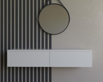 May include: A modern wall-mounted vanity with a round mirror. The vanity is white with two drawers, and the mirror has a black frame. The background features a vertical striped accent wall in gray and a neutral-toned wall.