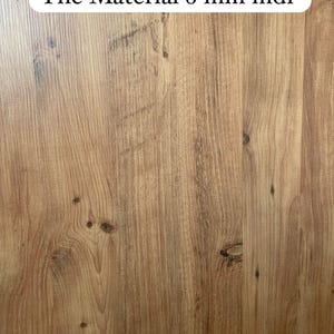 Pu&ograve; includere: Primo piano di una superficie a grana di legno con il testo "The Material 8 mm mdf" stampato su un adesivo ovale bianco.