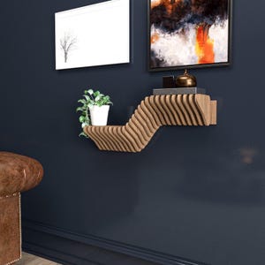 Pu&ograve; includere: Un ripiano a muro in legno con un design ondulato. Il ripiano &egrave; in legno marrone chiaro e ha una finitura naturale. &Egrave; montato su una parete blu scuro e ha una piccola pianta in vaso sullo scaffale superiore.