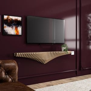 May include: A modern, floating wooden shelf with a unique, wave-like design, mounted on a deep burgundy wall. The shelf is made of alternating light and dark wood strips. A flat-screen TV is mounted above the shelf, and a small potted plant sits on the right side.