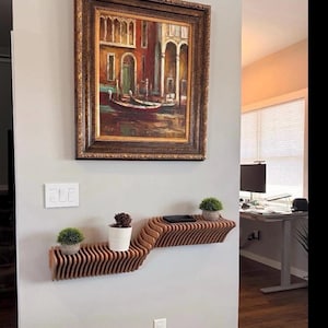 Pu&ograve; includere: Un ripiano a muro in legno con un design ondulato. Il ripiano &egrave; montato su una parete bianca e ha due piante in vaso. Un dipinto incorniciato di una scena di canale &egrave; appeso sopra il ripiano.