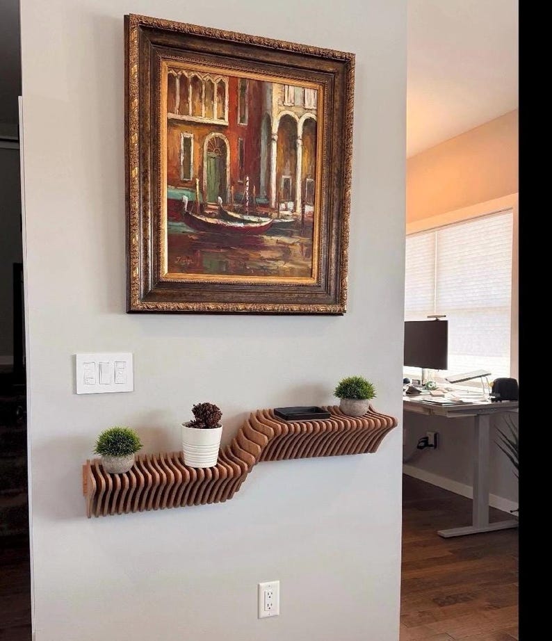 Pu&ograve; includere: Un ripiano a muro in legno con un design ondulato. Il ripiano &egrave; montato su una parete bianca e ha due piante in vaso. Un dipinto incorniciato di una scena di canale &egrave; appeso sopra il ripiano.