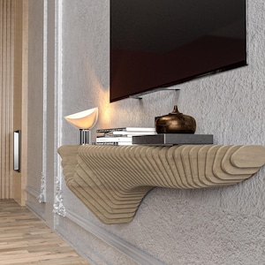 Pode incluir: Uma prateleira de parede de madeira com um design &uacute;nico em forma de onda. A prateleira &eacute; montada em uma parede e tem uma superf&iacute;cie plana para exibir objetos. H&aacute; livros, uma l&acirc;mpada e um objeto decorativo na prateleira.