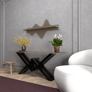 Op de afbeelding: Een zwarte metalen consoletafel met een houten blad en een geometrisch ontwerp. De tafel is versierd met een vaas met gele bloemen en een potplant. Een witte fauteuil staat op de achtergrond.