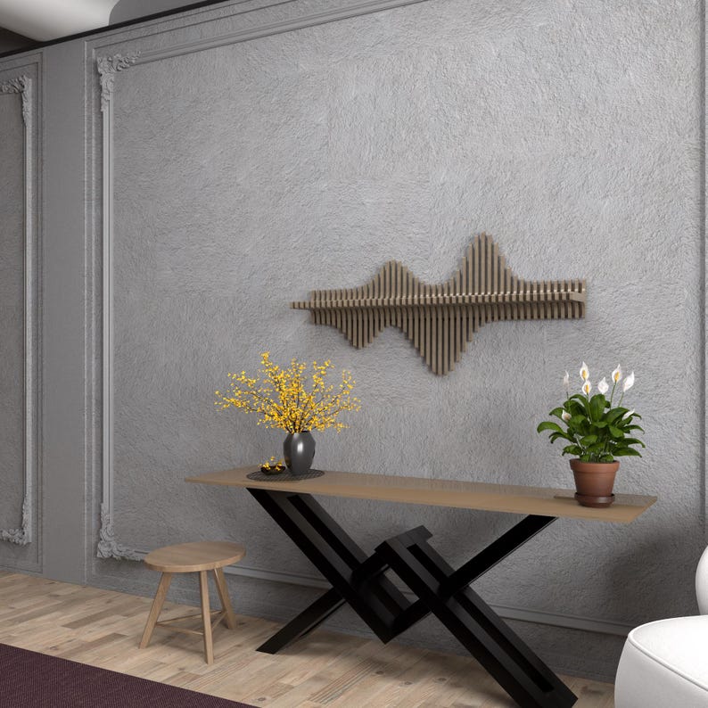 Op de afbeelding: Een houten wandplank met een golfvormig ontwerp. De plank is gemonteerd aan een grijze muur boven een zwarte metalen consoletafel met een houten blad. Er staan twee kleine potplanten op de tafel, een met gele bloemen en een met witte bloemen.
