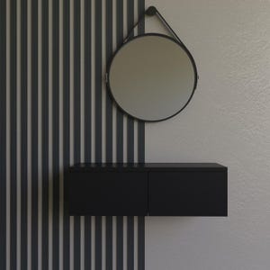 May include: A modern black wall-mounted vanity with two drawers, a round mirror, and a black frame. The mirror hangs from a black strap. The wall behind the vanity is divided into vertical gray and white panels.