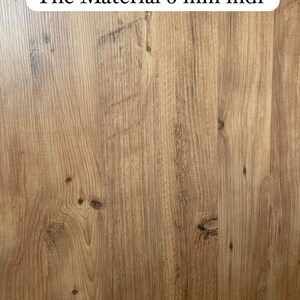 Pode incluir: Close-up de uma superf&iacute;cie de gr&atilde;o de madeira com o texto "The Material 8 mm mdf" impresso em um adesivo oval branco.